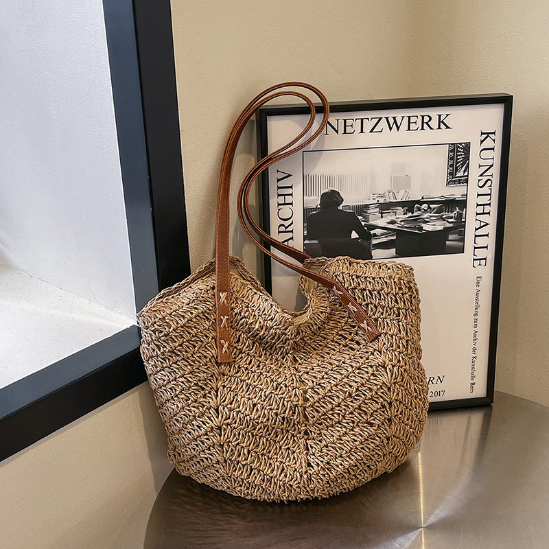 Woven handbag with brown handle on a surface next to a framed picture