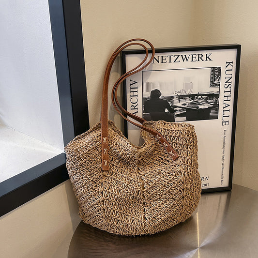 Woven handbag with brown handle on a surface next to a framed picture