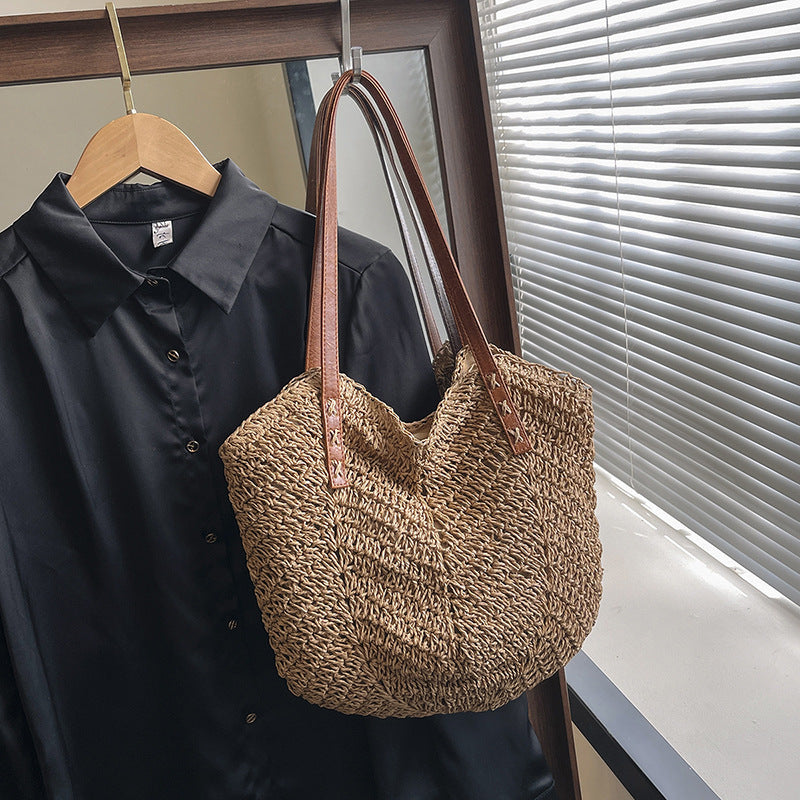 Woven beige bag with brown handles hanging on a black shirt against a window background