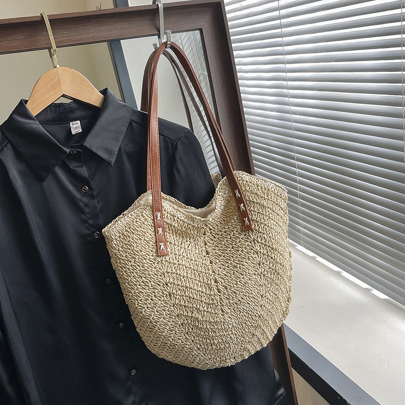 Woven beige tote bag with brown handles hanging on a black shirt against a window background