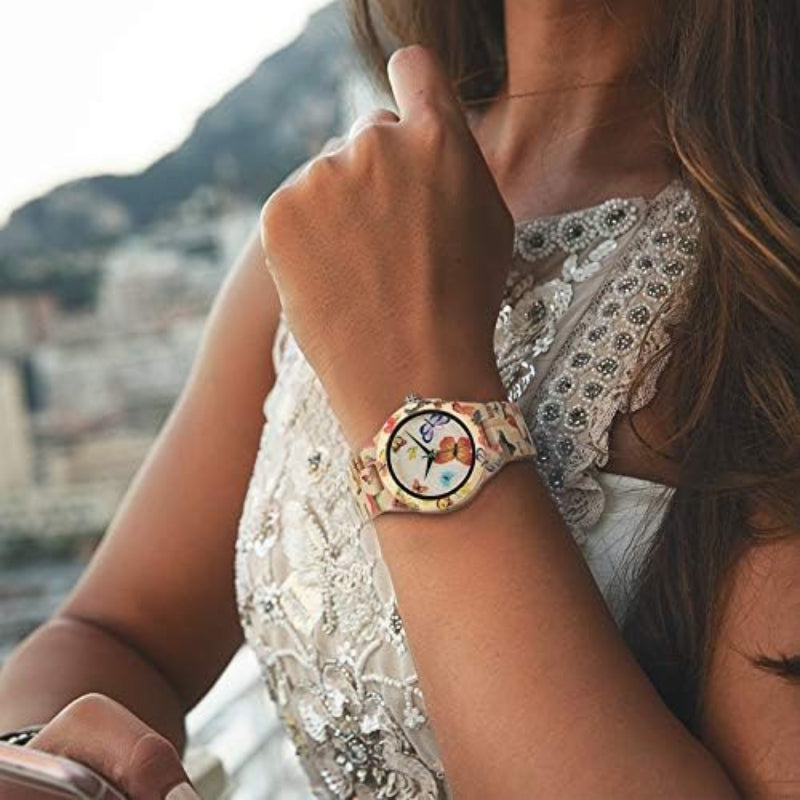 A close-up lifestyle shot of a woman wearing a colorful wrist watch with a patterned strap and a round face, set against a blurred outdoor background.