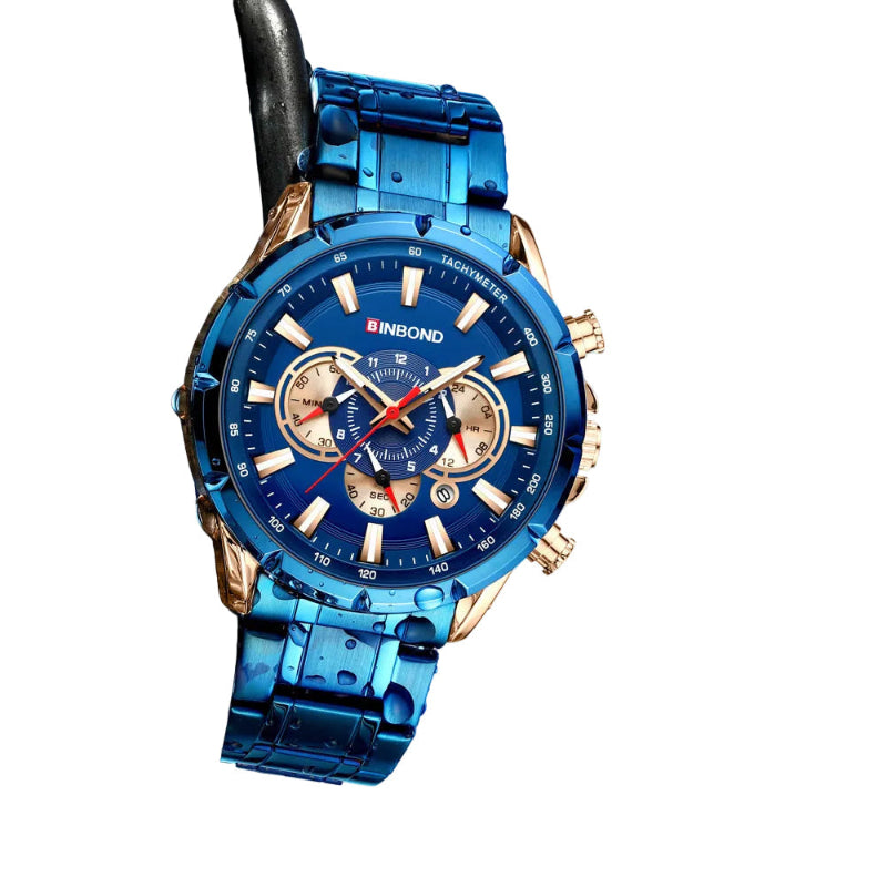 A blue and rose gold men's analog watch with a metallic link band, resting on a black chain against a blurred water background.