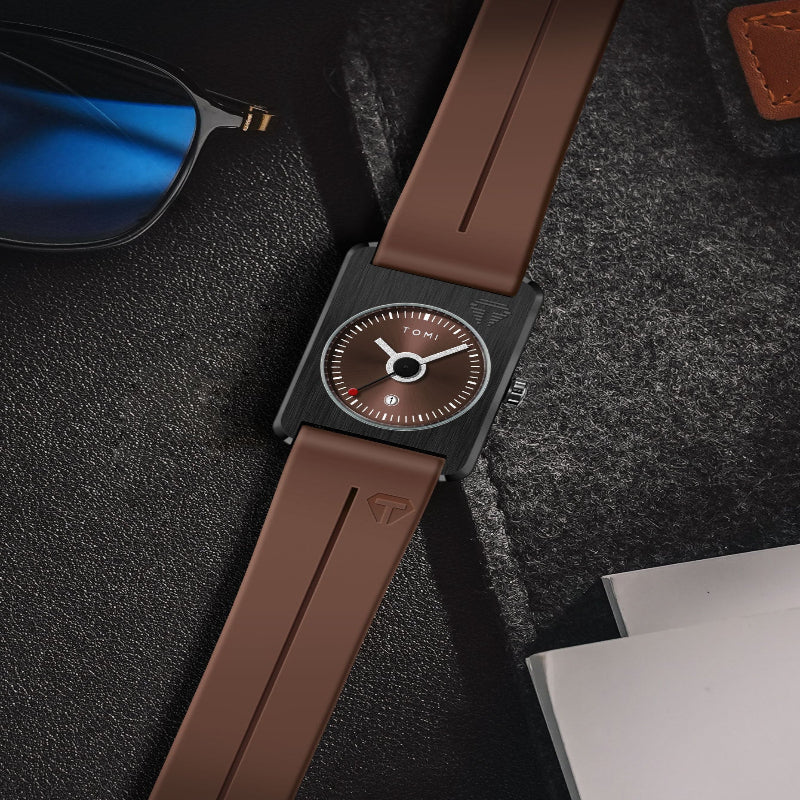Watch with a brown strap on a textured surface with sunglasses and a leather wallet.