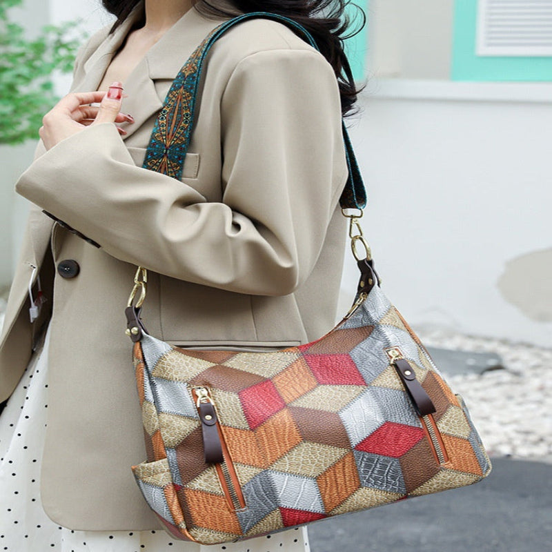 A woman wearing a beige blazer carries a large geometric patchwork shoulder bag with brown, red, orange, and gray panels, shown in an outdoor setting with text at the top reading 'MODEL DISPLAY Fashionista Styling Show'.