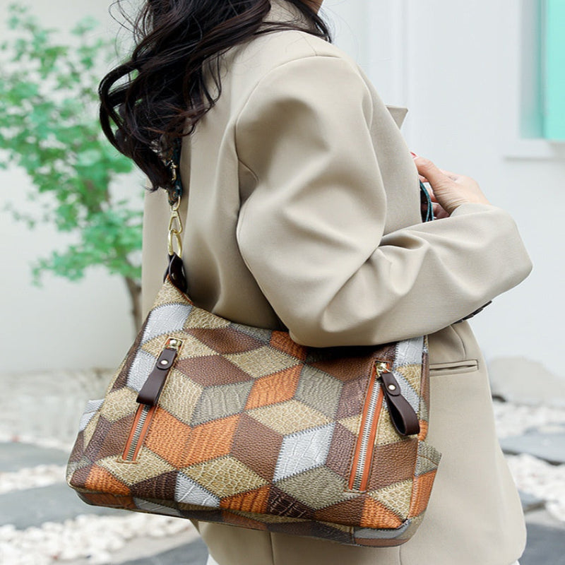 A woman wearing a beige blazer and white polka-dot skirt carries a large geometric pattern shoulder bag with brown leather trim and gold-tone hardware.