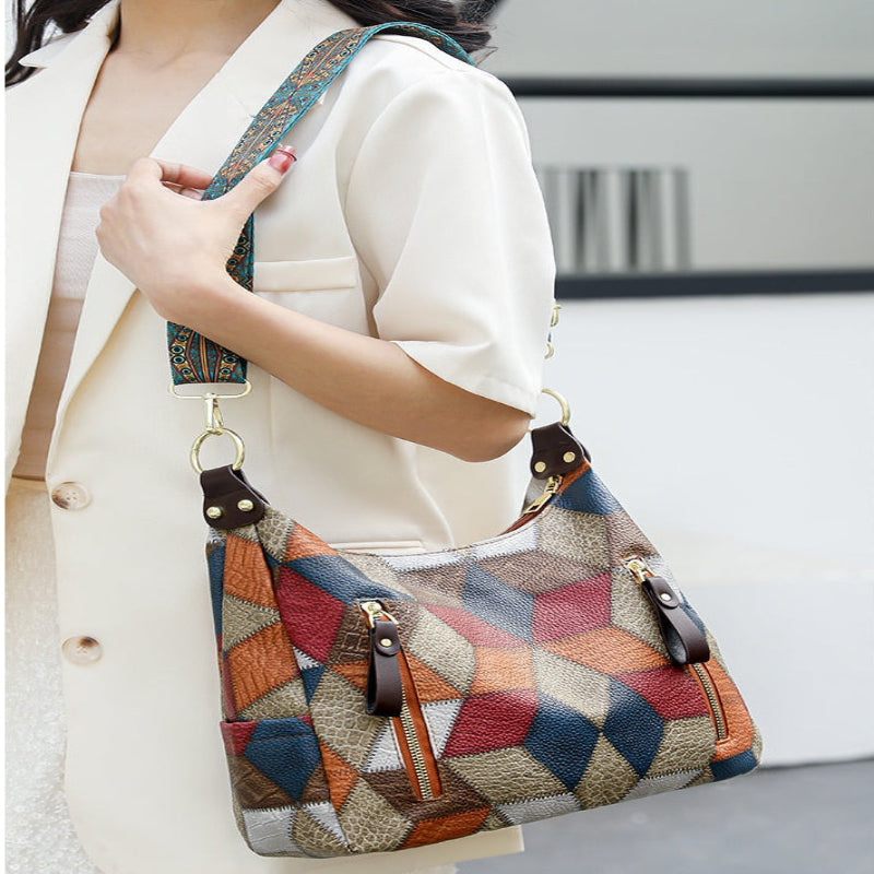 A woman wearing a cream-colored blazer carries a geometric patterned shoulder bag with a multicolor diamond design in blue, red, orange, and beige, featuring brown leather accents and a patterned strap.