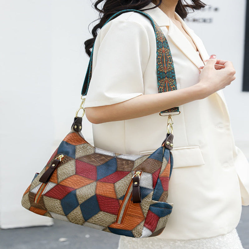 A woman wearing a cream-colored blazer carries a large, colorful geometric patchwork shoulder bag with brown leather trim and gold-tone hardware.