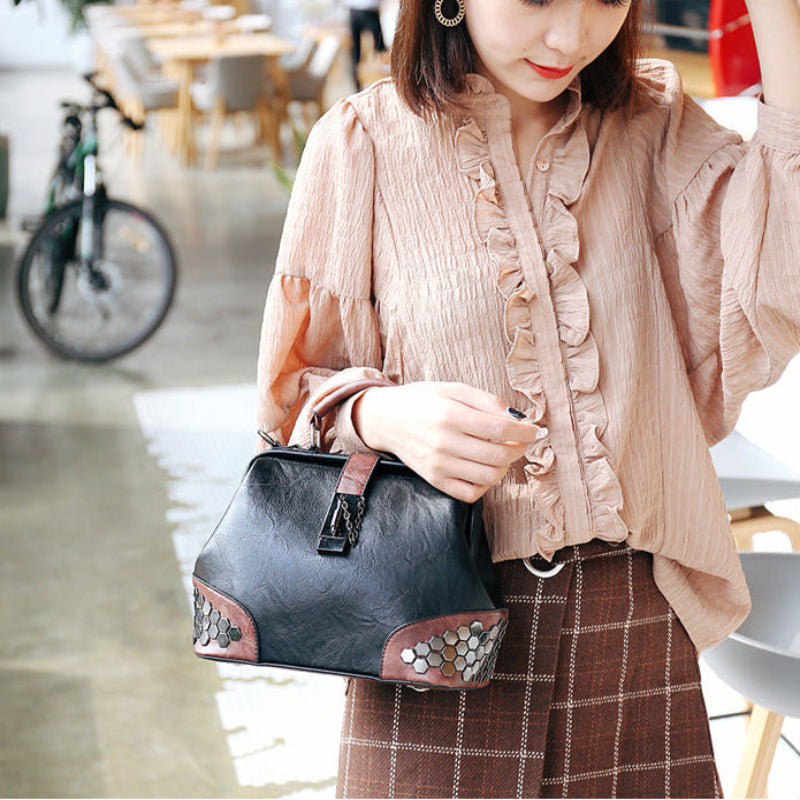Woman holding a black handbag with decorative elements in an outdoor setting