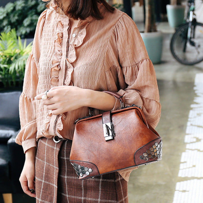 Person holding a brown leather handbag in an outdoor setting