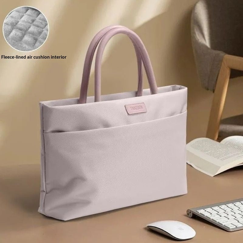 A light lavender-gray fabric tote bag with dual top handles, shown on a desk with a mouse, keyboard, and open book in a styled indoor setting. A circular inset in the top-left shows the quilted air cushion interior.