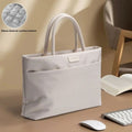 A light gray tote bag with dual top handles, shown on a desk with an open book, keyboard, and mouse. The image includes a circular inset showing the bag's quilted fleece-lined interior.
