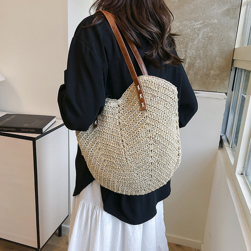 Person wearing a large woven bag with a brown strap indoors.